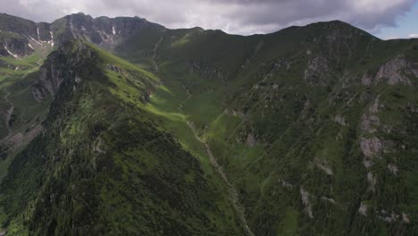 Lush-Tiganesti-Valley-in-Bucegi-Mountains-under-a-dynamic-sky,-aerial-view