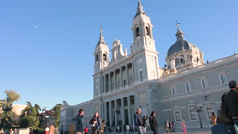 Tourists-and-locals-walk-through-the-Armeria-plaza-in-front-of-the-Roman-Catholic-Almudena-Cathedral,-completed-and-consecrated-in-1993-by-Pope-John-Paul-II-in-Madrid,-Spain