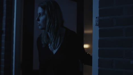 Worried-woman-opening-front-door-of-her-home-and-looking-around-at-night