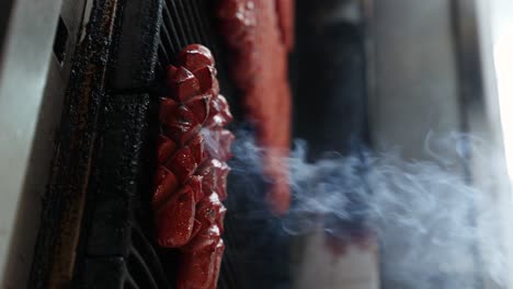 Person-use-metal-tongs-to-move-hotdog-sausages-on-grill-grate,-vertical-video