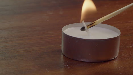 Full-frame-closeup-of-wooden-match-lighting-single-tea-candle-on-table
