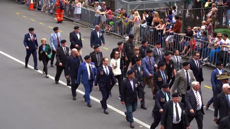 Eine-Gruppe-Von-Männern-Und-Frauen-Marschiert-Während-Der-Jährlichen-Anzac-Day-Parade-Die-Straße-Entlang-Und-Zollt-Den-Kriegshelden-Tribut,-Während-Am-Rande-Die-Menge-Jubelt