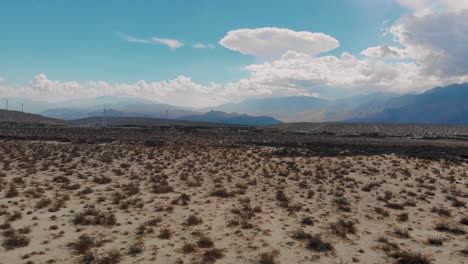 Slow-fly-over-pulling-back-of-sand-and-brush-covered-hills-near-small-desert-town