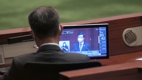 A-lawmaker-listens-and-watches-from-a-screen-Hong-Kong's-chief-executive,-John-Lee-Ka-chiu,-delivering-the-annual-policy-address-at-the-Legislative-Council-building-in-Hong-Kong