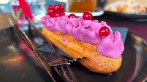 Delicioso-Eclair-Con-Crema-De-Bayas-Del-Bosque-En-Un-Plato-En-Una-Panadería,-Masa-Choux-Rellena-De-Crema-Morada,-Postre-Dulce,-Toma-De-4k