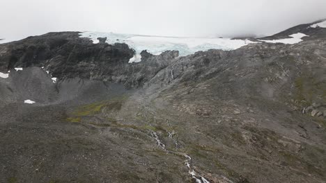 a-large-glacier-on-a-rocky-mountain-with-some-small-waterfalls-and-rivers-in-a-foggy-environment,-norway,-europe,-drone