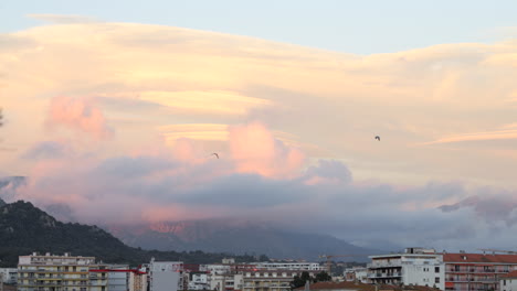 Beautiful-view-of-Ajaccio-at-sunset,-birds-flying-in-sky-with-colorful-clouds
