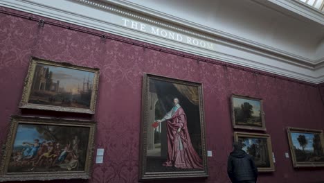 Visitor-Walking-Past-Large-Painting-Hanging-On-Wall-In-The-Mond-Room-At-The-National-Portrait-Gallery-In-London