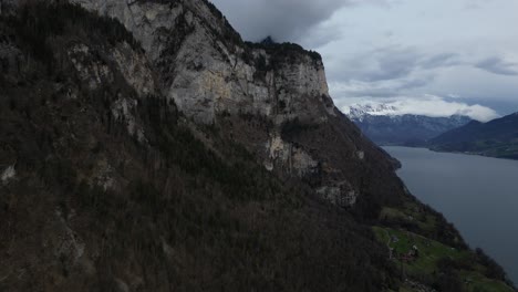 Drone-shot-of-snow-covered-mountains-by-the-cliff-of-hills-at-foreground-in-Walensee,-Switzerland