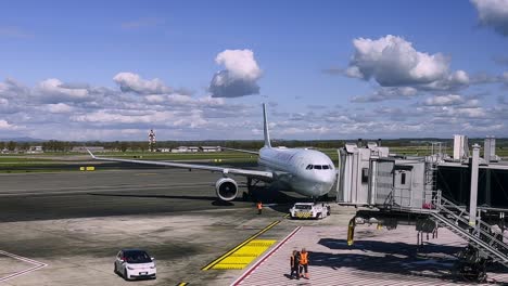 Pushback-truck-pushing-Air-Canada-aircraft-backward-departing-from-airport-terminal-gate-with-loading-bridge-detached-and-ground-operators-at-work-on-tarmac