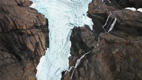 Un-Enorme-Glaciar-Entre-Las-Montañas-Con-Una-Cascada-Desde-Arriba,-Briksdalsbreen,-Noruega,-Naturaleza,-Drone