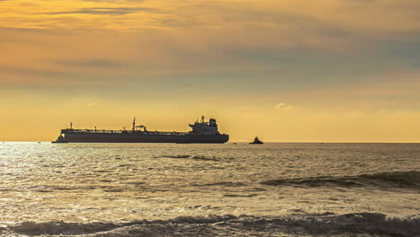 Massive-cargo-vessel-moored-near-coastline-during-sunset,-time-lapse-view