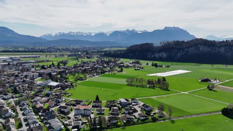 Oberriet-in-switzerland-with-lush-green-fields-and-alps-backdrop,-sunny-day,-aerial-view