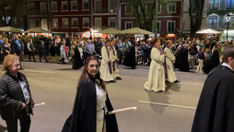 Vemos-A-Los-Sacerdotes-En-La-Procesión,-Uno-De-Ellos-Viste-Diferente-Vestimenta-Color-Violeta,-Hay-Acólitos-Portando-Cruces-Y-Cirios-Y-Muchos-Fieles-En-Filas,-Gran-Afluencia-De-Público