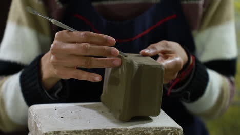 Close-up-over-the-hands-of-a-mexican-craftswoman-giving-details-to-a-square-shaped-clay-craft