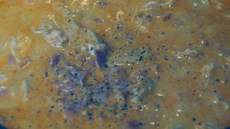 Full-frame-close-up:-Black-pepper-is-added-to-simmering-meaty-stew