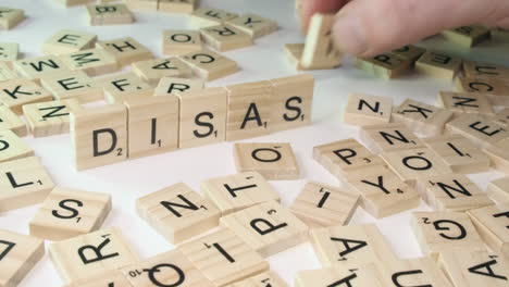 Game-letter-tiles-placed-on-edge-by-hand-form-word-DISASTER,-Scrabble