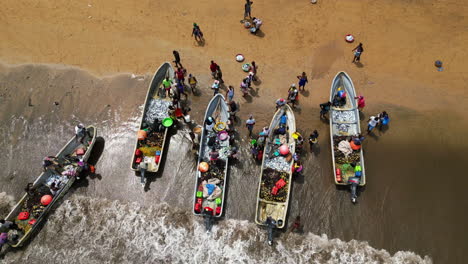 Toma-De-ángulo-Alto-De-Pescadores-Africanos-Llegando-A-Una-Playa-Con-Barcos-Llenos-De-Peces.