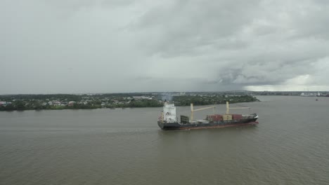 Cargo-ship-sailing-in-the-Suriname-river-towards-harbor,-drone-view-ascending
