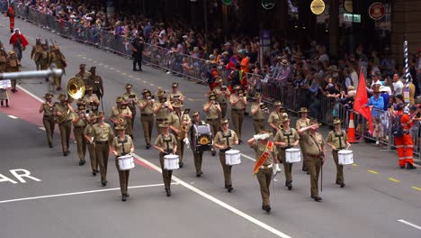 Cuerpo-De-Banda-Del-Ejército-Australiano-Tocando-Instrumentos-Musicales-Y-Marchando-Por-La-Calle,-Alentado-Por-La-Multitud-Que-Se-Alineaba-A-Los-Lados-Durante-El-Desfile-Del-Día-De-Anzac.