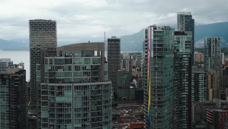 close-up-aerial-shot-going-backward-between-buildings-in-Vancouver-city,-yaletown,-with-mountains-and-ocean-in-the-background-on-an-overcast-day