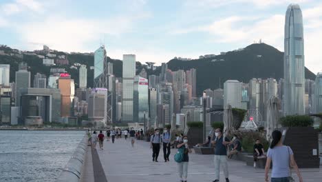 Menschen-Schlendern-Durch-Die-Victoria-Waterfront,-Während-Im-Hintergrund-Die-Skyline-Von-Hongkong-Zu-Sehen-Ist