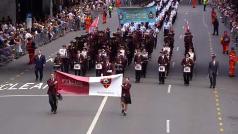 Estudiantes-De-La-Banda-De-Música-Indooroopilly-De-St-Peters-Lutheran-College-Tocando-Y-Marchando-Por-La-Calle-Con-Multitudes-Aclamando-Al-Lado,-Honrando-La-Memoria-De-Aquellos-Que-Sirvieron-Durante-El-Día-De-Anzac.