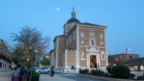 filming-with-a-camera-turn-of-the-parish-of-Nuestra-Señora-de-las-Angustias-with-the-full-moon-next-to-its-dome,-the-posters-on-the-façade-and-the-expected-moment-is-approaching,-the-people-arrive