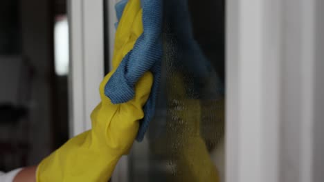 Woman,-housework-and-housekeeping-concept---woman-in-gloves-cleaning-window-with-rag-and-cleanser-spray-at-home