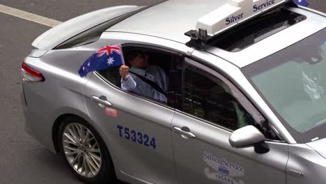 A-woman-waving-the-Australian-national-flag-from-the-window-of-a-Silver-service-cab-during-Anzac-Day-parade-in-Brisbane-city,-close-up-shot