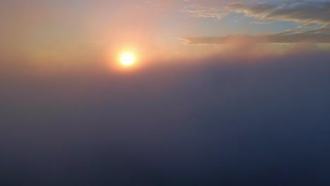 Drone-camera-is-raising-up-from-the-thick-fog-to-above-ocean-of-clouds-at-sunrise-time