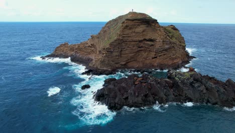 Aerial-view-circling-small-offshore-island-Ilheu-mole-and-lighthouse-North-west-coast-of-Porto-Moniz,-Madeira,-Portugal