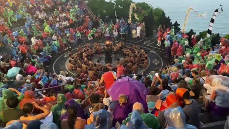 A-large-crowd-of-tourists-watch-a-Kecak-dance-performance-wearing-raincoats-at-Uluwatu-Temple,-Bali,-Indonesia-despite-a-rainstorm