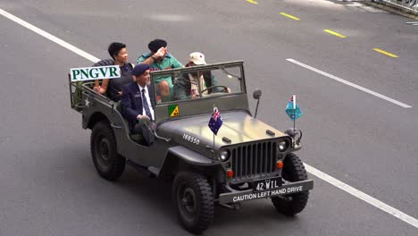 Familia-Y-Representantes-De-La-Unidad-De-Fusileros-Voluntarios-De-Papúa-Nueva-Guinea-Viajando-En-El-Vehículo-Militar-Jeep-Conduciendo-Por-La-Calle-Durante-El-Desfile-Del-Día-De-Anzac-En-La-Ciudad-De-Brisbane.