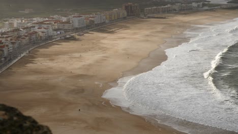 Praia-da-Nazaré-beach-in-golden-hour-with-shadows-shot-from-above-in-4k-with-distant-people-walking-on-beach