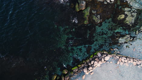 Drone-rises-above-rock-wall-at-edge-of-beach-in-Newport-Rhode-Island