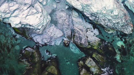 Drone-top-down-pan-across-chalky-white-rocks-as-ocean-waves-crash-in-water