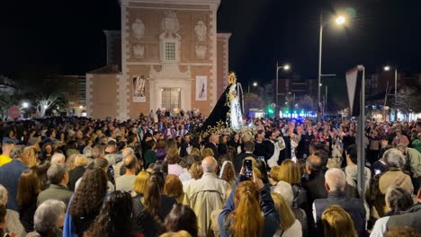 Vemos-La-Parroquia-Iluminada,-La-Virgen-Siendo-Llevada-Por-Sus-Feligreses,-El-Cura-Detrás-De-Ella-Y-Una-Gran-Multitud-Entusiasmada-Por-La-Procesión