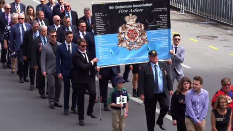 Stolze-Vertreter-Und-Ihre-Familien-Vom-9.-Bataillon-Marschieren-Als-Erste-An-Land-Die-Straße-Entlang-Und-Nehmen-An-Der-Tradition-Der-Anzac-Day-Parade-Teil,-Um-Diejenigen-Zu-Ehren,-Die-Gedient-Haben