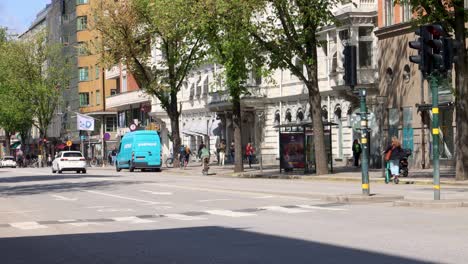 Bike-and-car-traffic-on-tree-lined-street-in-central-Stockholm,-sunny-summer-day