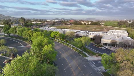 East-Brier-Drive-San-Bernardino-California-early-in-the-morning-sunrise-lighting-on-lush-green-vegetation-with-a-blue-sky-and-commercial-buildings-in-the-background-AERIAL-DOLLY