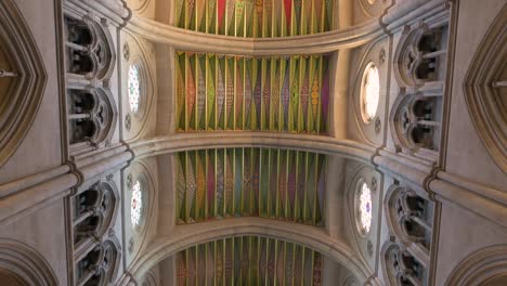 Tilting-down-shot-interior-view-of-the-Roman-Catholic-Almudena-Cathedral-and-ceiling-fresco-paintings-as-arches,-columns,-and-pillars-decorate-and-support-the-ceiling-and-dome