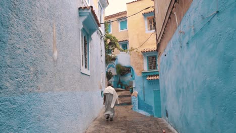 Un-Hombre-Marroquí-Mayor-Y-Bajo-Con-Ropa-Tradicional-Caminando-Por-Una-Hermosa-Calle-En-Chefchaouen,-Marruecos