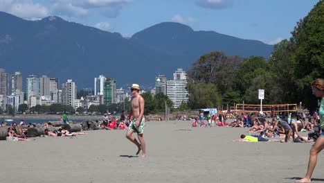 A-man-with-a-cowboy-hat-walks-on-a-beach-with-sunbathers