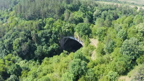 Drone-panning-from-the-right-to-the-left-side-of-the-frame,-above-the-entrance-of-Prohodna-Cave,-also-called-Gods-Bridge,-located-in-Karlukovo,-in-Bulgaria