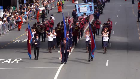 Parade-music-band-marching-down-the-street,-cheered-on-by-crowds-lining-the-sides-during-Anzac-Day