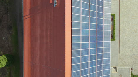 A-top-down-aerial-shot-showcases-a-vast-array-of-blue-solar-panels-neatly-arranged-on-a-building's-terracotta-rooftop,-highlighting-sustainable-energy-practices