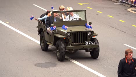 Veteranen-Und-Familien-Fahren-Auf-Dem-Militär-Oldtimer-Die-Straße-Entlang,-Nehmen-An-Der-Anzac-Day-Parade-In-Brisbane-Teil-Und-Schwenken-Der-Jubelnden-Menge-Die-Australische-Nationalflagge