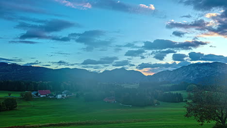 Colorful-time-lapse-landscape-austrian-alps-european-countryside-skyline-clouds-in-motion,-afternoon-turning-into-dusk,-sun-rays-over-farmers-green-village-fields