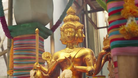 Primer-Plano-De-La-Escultura-De-La-Estatua-Dorada-De-Brahma-Phra-Phrom-4-Frente-A-Dios-En-Hindú-Y-Budismo-Alrededor-De-Un-Templo-Colorido,-Atmósfera-Religiosa-Hinduista